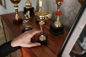 A close-up of a hand reaching for a shiny trophy on a wooden shelf, symbolizing success.